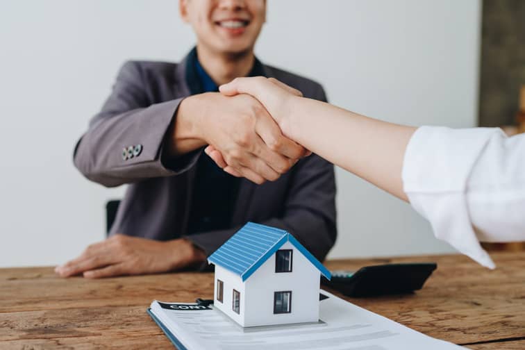 Un homme et une femme se serrent la main devant un contrat immobilier