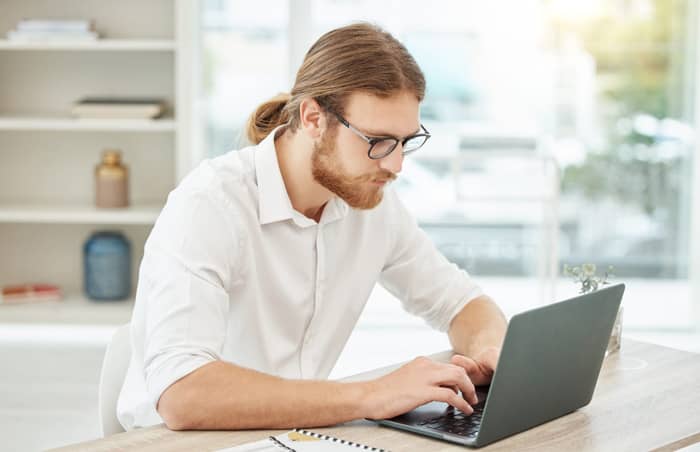 Un homme portant des lunettes utilise un ordinateur portable à un bureau